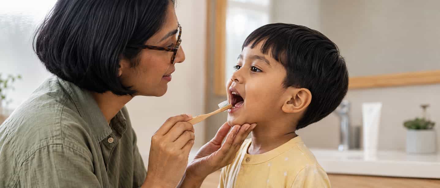 A parent brushing a young child’s teeth while supporting the chin