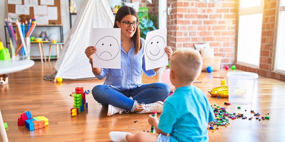 young therapist woman speaking with child, counselor and behaviour correction at the office showing happy and sad face