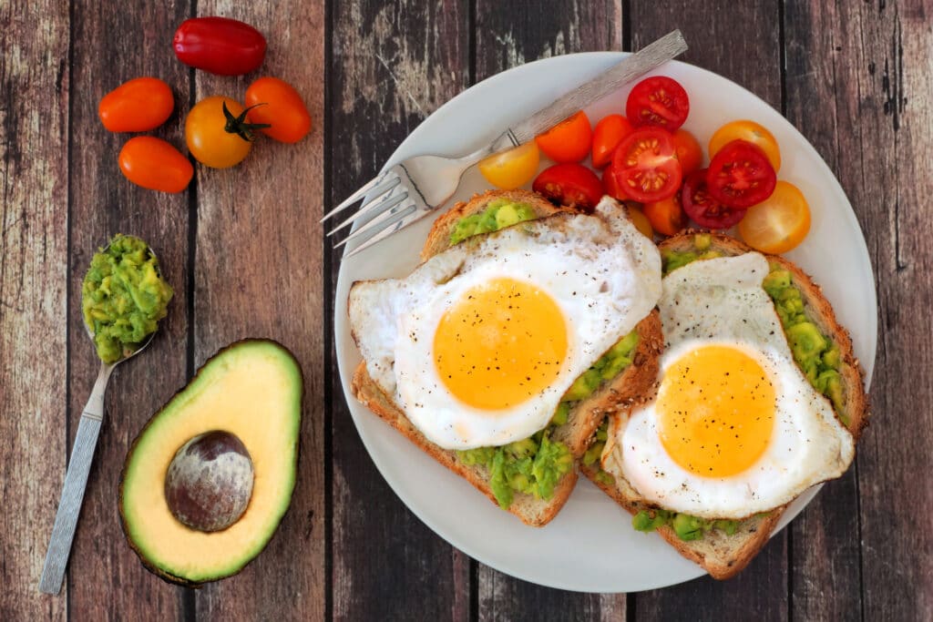 healthy avocado, egg toasts with tomatoes on rustic wood background