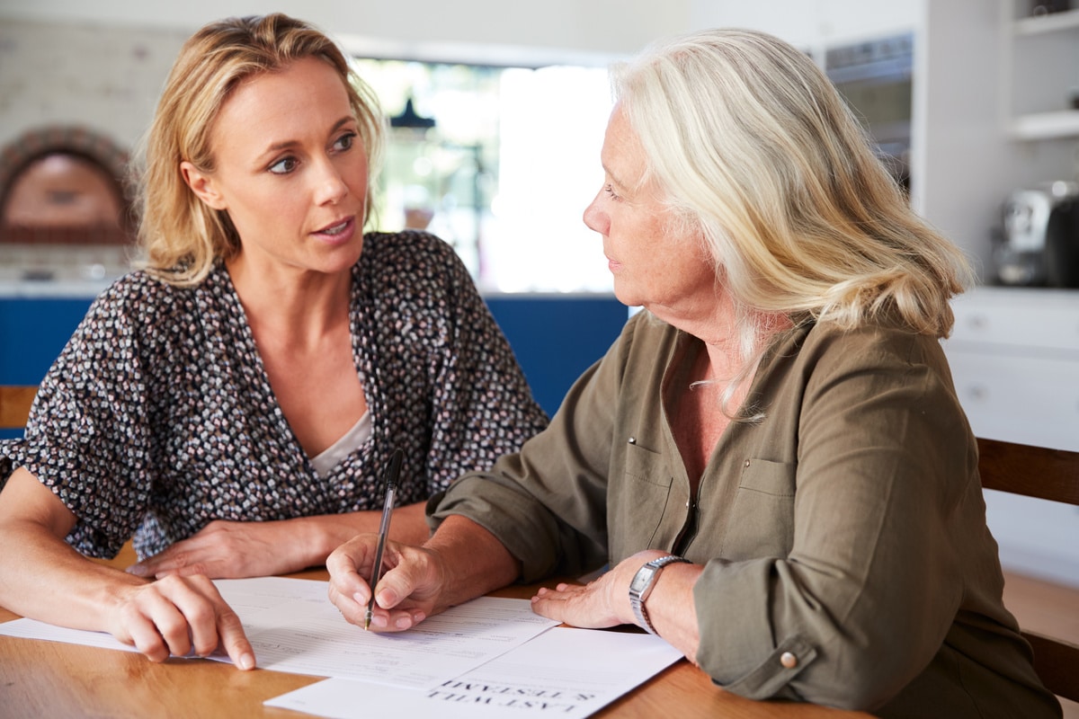 female friend helping senior woman to complete last will and testament at home