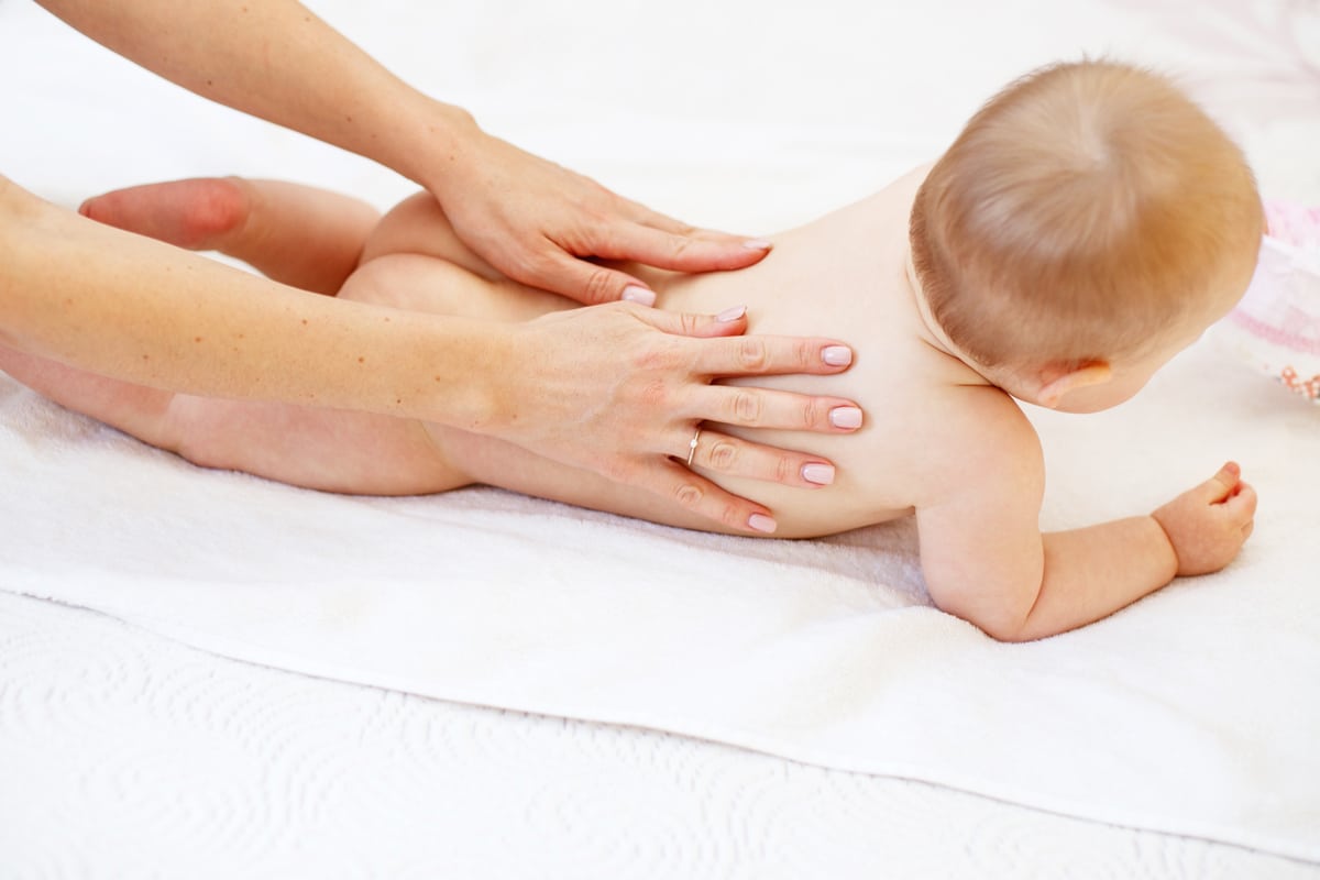 mother massaging baby in bed at home