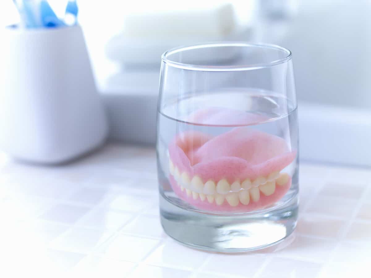 close up of dentures soaking in glass of water