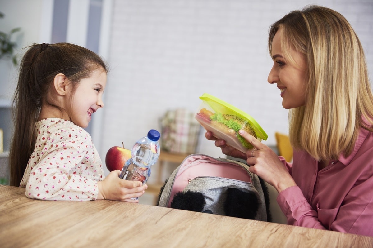 mum putting lunch box with healthy food in backpack