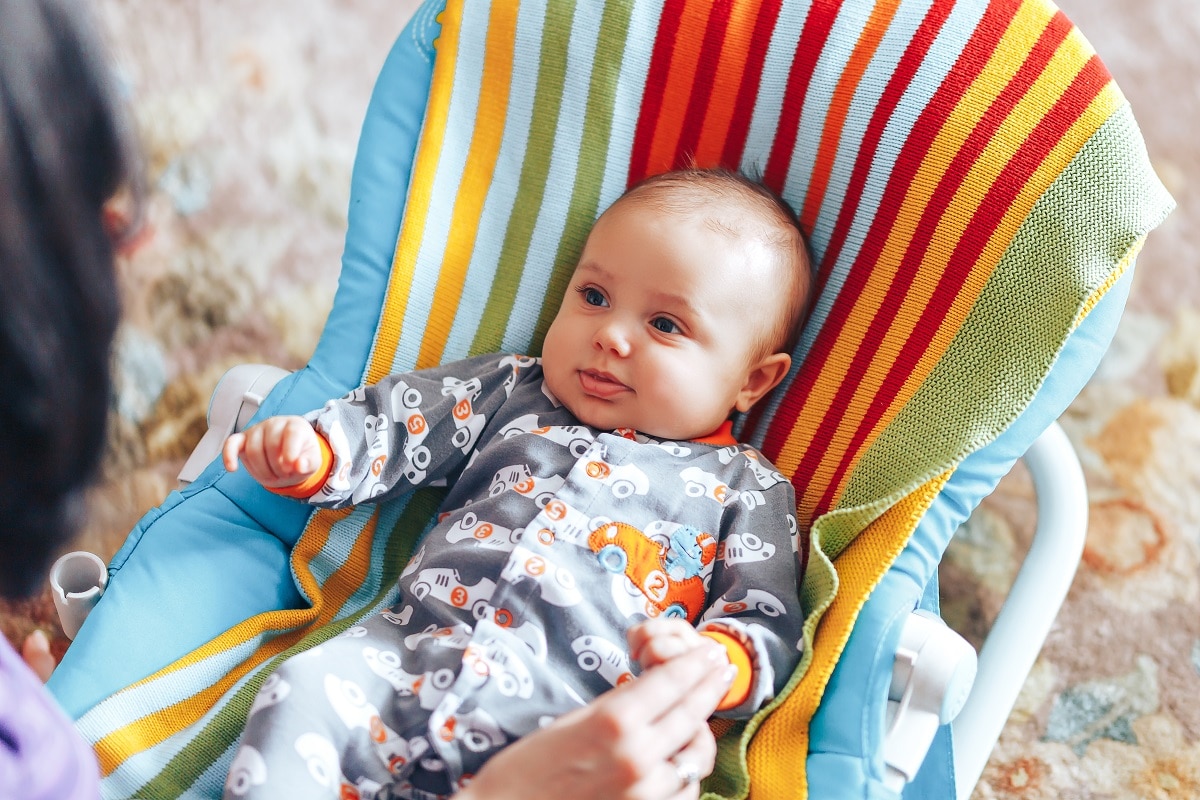 nice blue eyed baby child relaxing on a sunbed or a deck chair colored bouncer at home