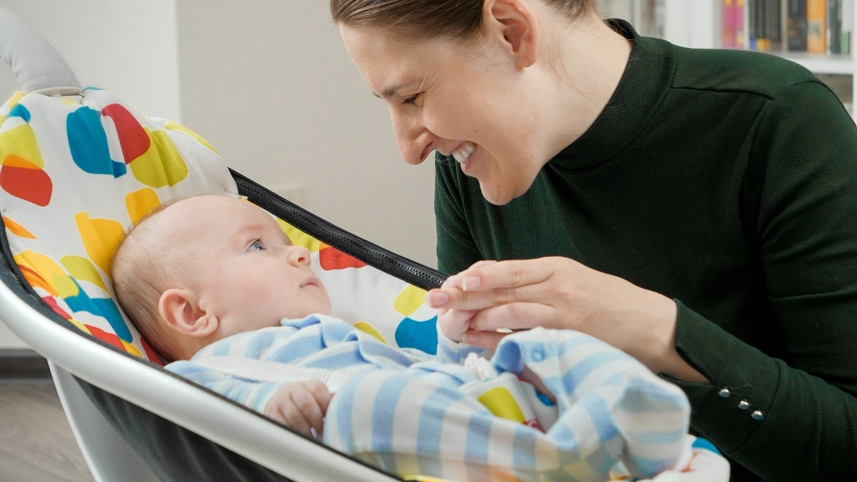 portrait of smiling mother looking at her cute baby son sitting in electric rocking chair. child development and happy parenting