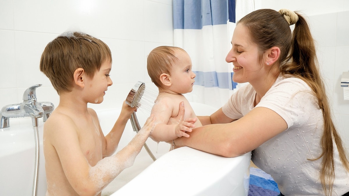 smiling boy with mother washing baby boy in bath under shower