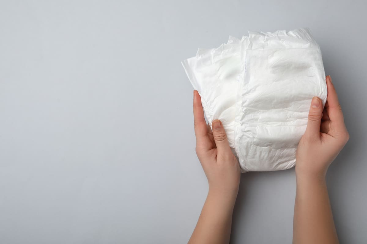 woman with diapers on light grey background, closeup. space for