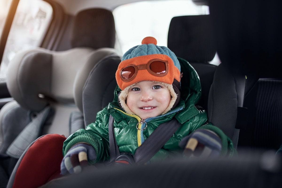 happy baby boy sitting in baby car seat. child in auto baby seat in car. ?hild is dressed in winter clothes and a hat.