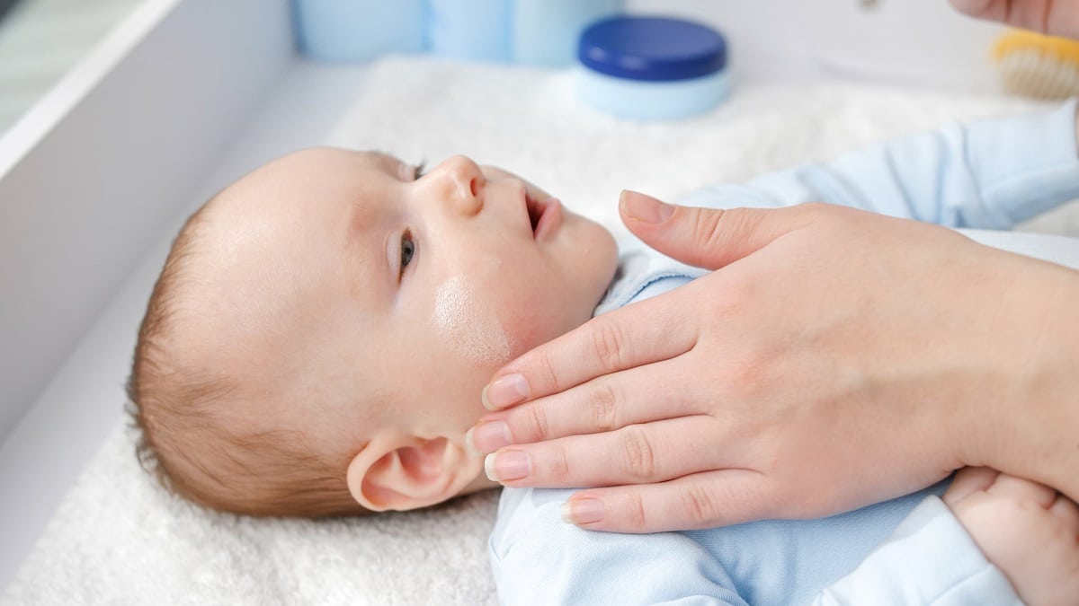 mother using creme and lotion to prevent her baby skin from drying. concept of hygiene, baby care and healthcare