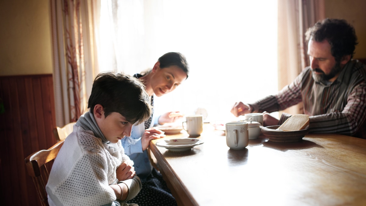 angry small girl with parents sulking indoors at the table at home, poverty concept.