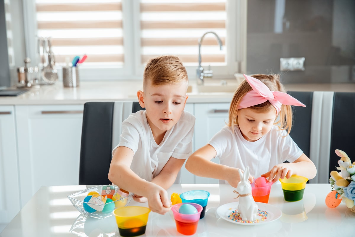 children paint easter eggs while sitting at the kitchen table
