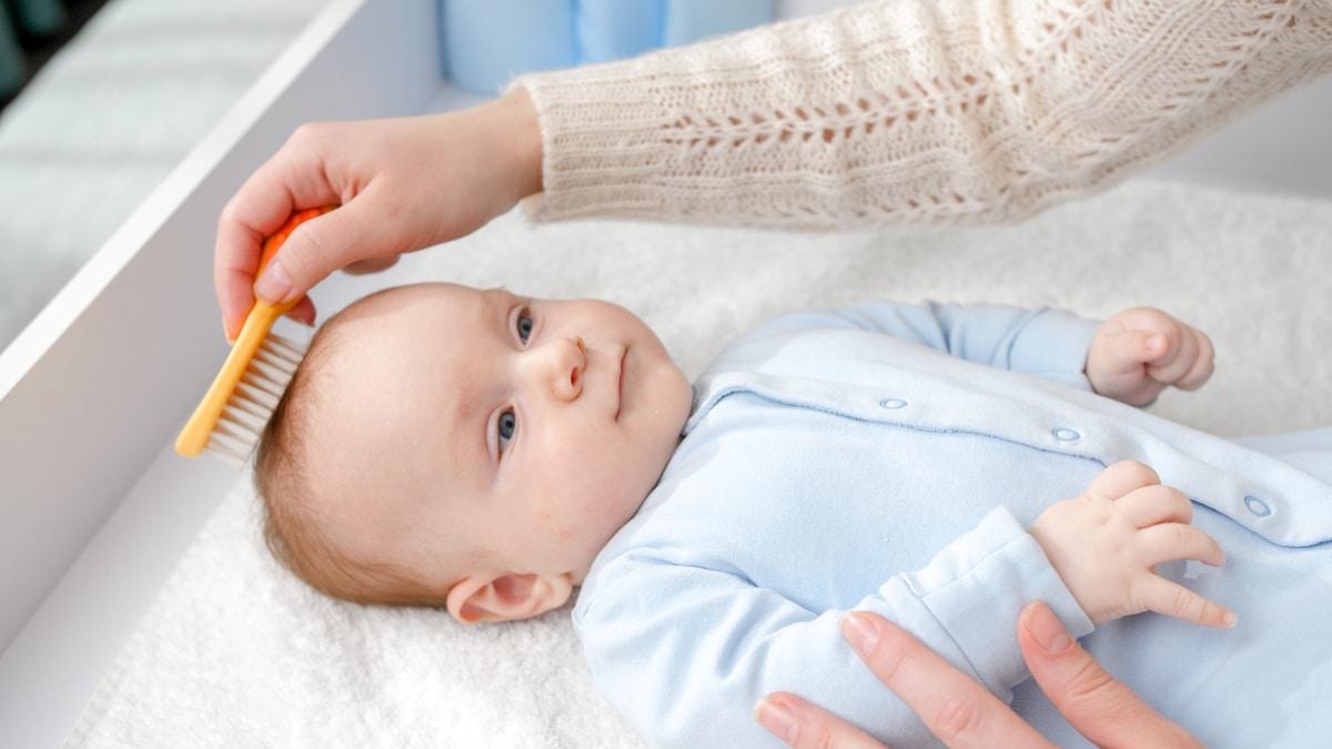 closeup of young mother combing her baby son hair with hair brush. concept of hygiene, baby care and healthcare.