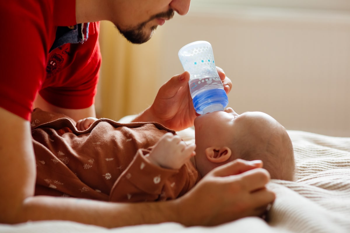 father feeding baby on bed