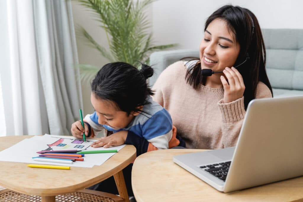 happy asian mother working on computer at home with her child busy family mom giving call center support focus on kid right hand