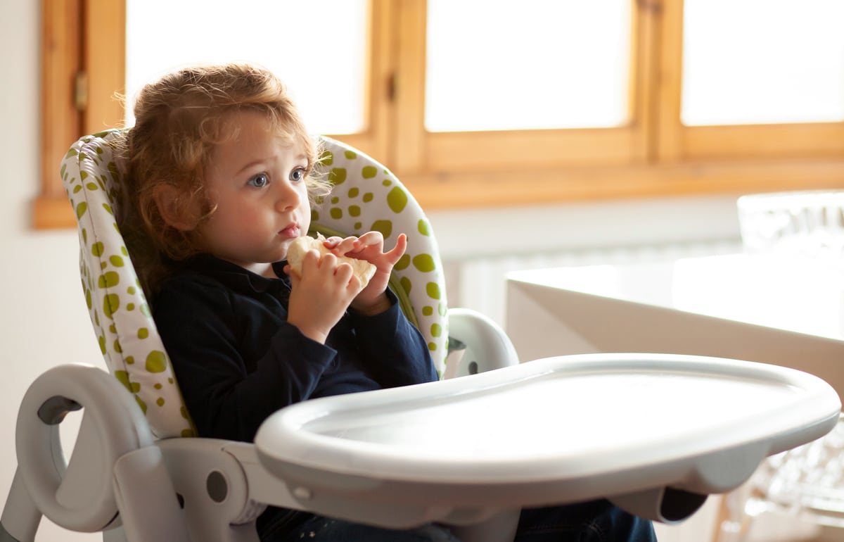 little girl eats bread in the high chair