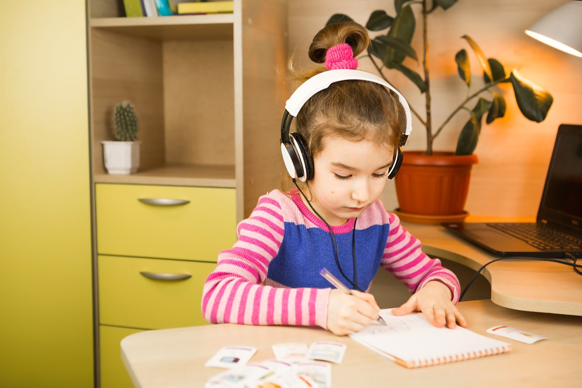 a pre school girl with headphones is engaged at home at the tabl