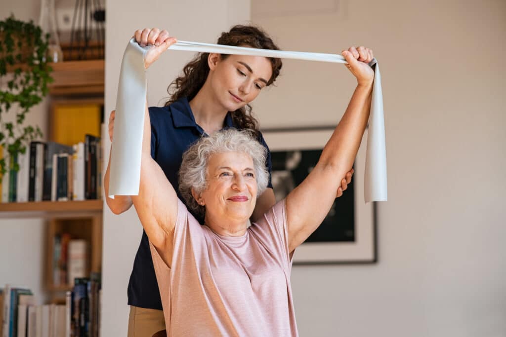 senior patient doing exercise with elastic band at home with per