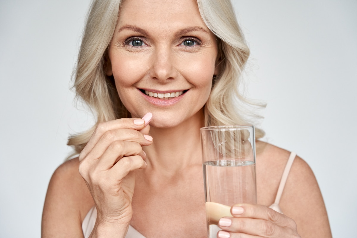 smiling healthy middle aged 50s woman taking supplement vitamin pill.