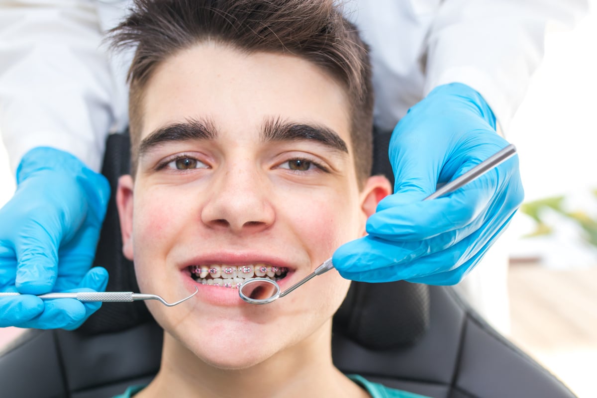 dentist with tools in the young man's mouth with orthodontics