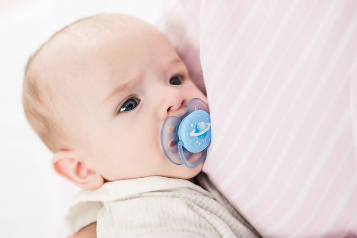 partial view of little baby with pacifier on mothers hands