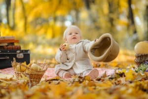 little cute girl sits on a plaid, eats an apple and holds out a hat. autumn photo shoot