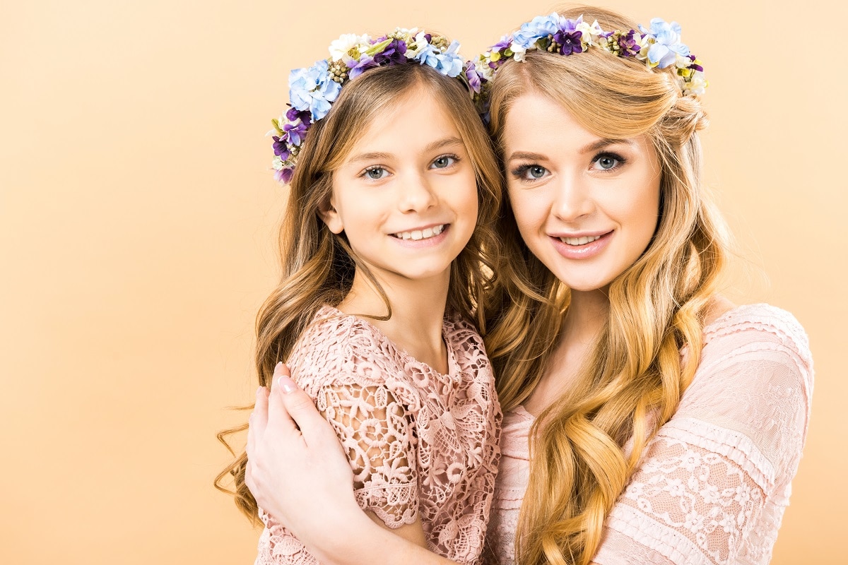 cute child and pretty mom in colorful floral wreaths embracing and looking at camera on yellow