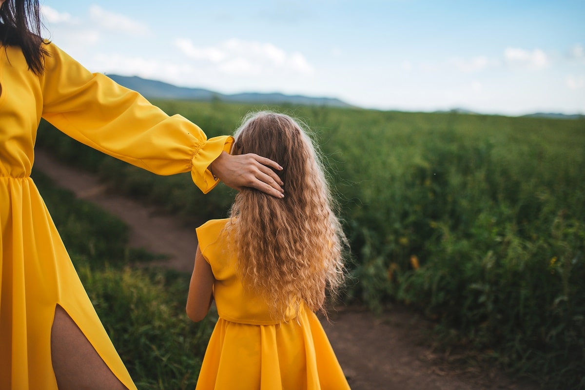 mom and daughter in yellow dresses standing in the open air on a background of grass