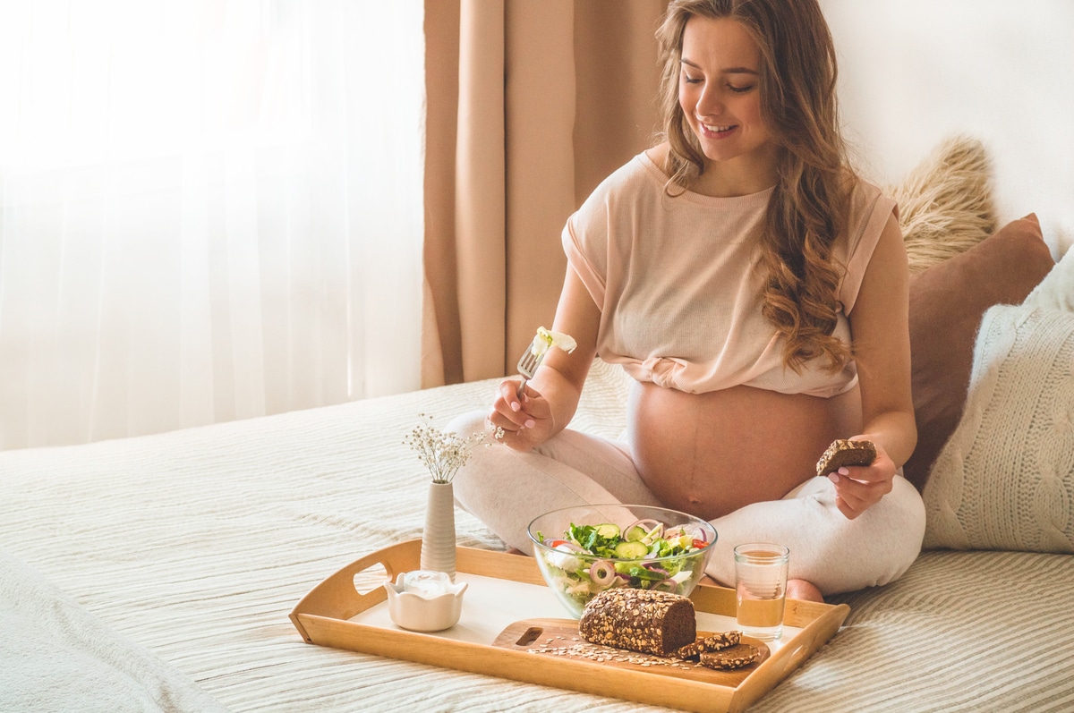 pregnancy and healthy organic nutrition. pregnant woman enjoying fresh vegetable salad in bed, free space