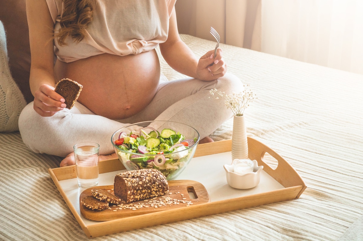 pregnancy and healthy organic nutrition. pregnant woman enjoying fresh vegetable salad in bed, free space