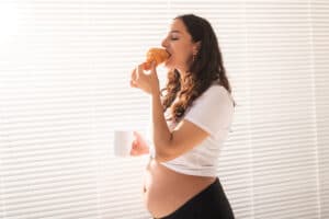 pregnant woman eating croissant and drinks coffee. pregnancy and maternity leave