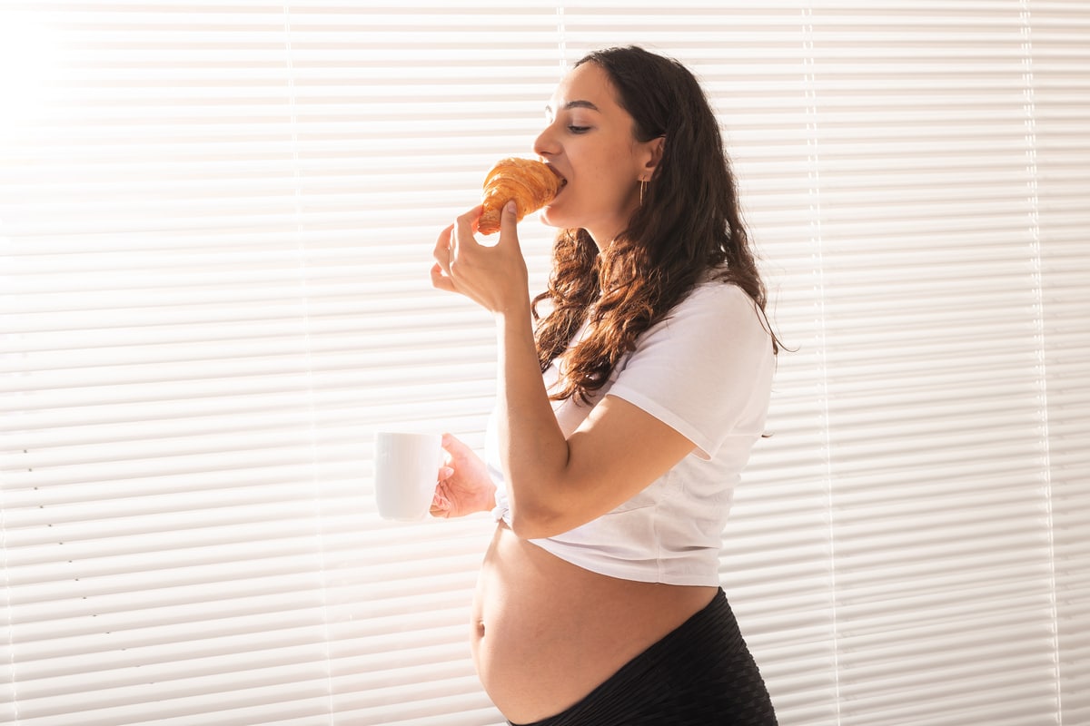 pregnant woman eating croissant and drinks coffee. pregnancy and maternity leave