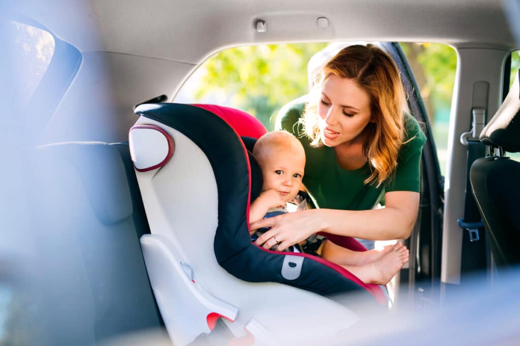 young mother putting baby boy in the car seat.