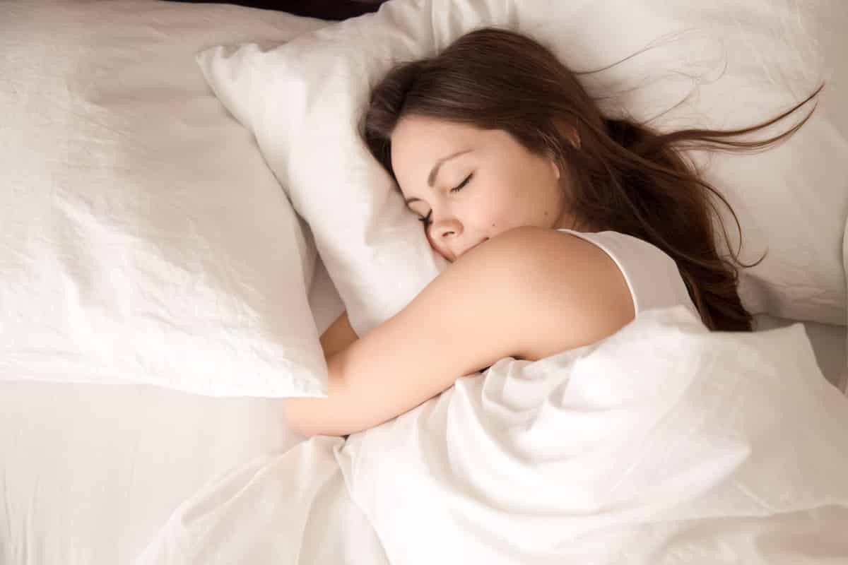 woman sleeping in bed hugging soft white pillow