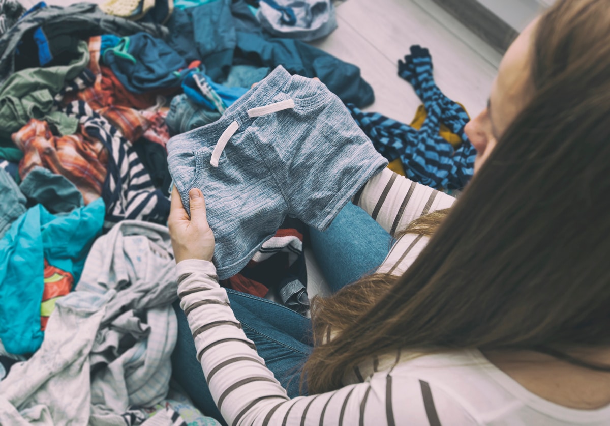 the pregnant woman is sorting baby clothes