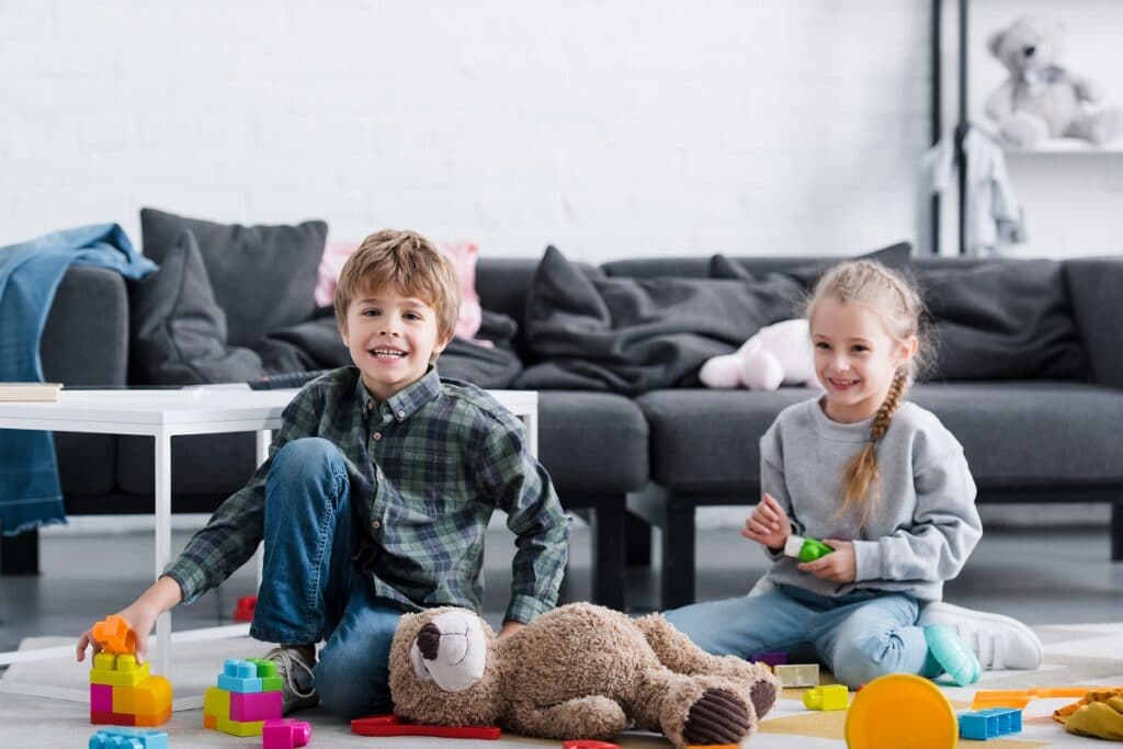 adorable happy children sitting on floor and playing with toys at home