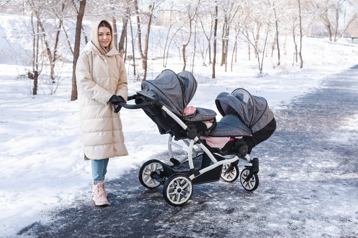 young mother with double baby stroller for twins walking outside in winter