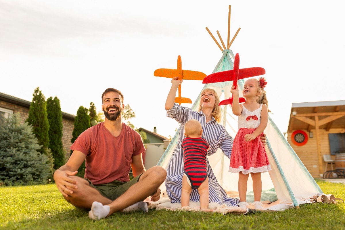 parents playing with children, throwing toy airplanes while camp