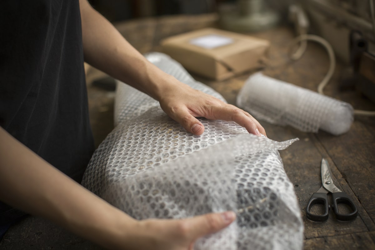 a woman wrapping an item in bubble wrap, a parcel being prepared for despatch.,packaging and delivery