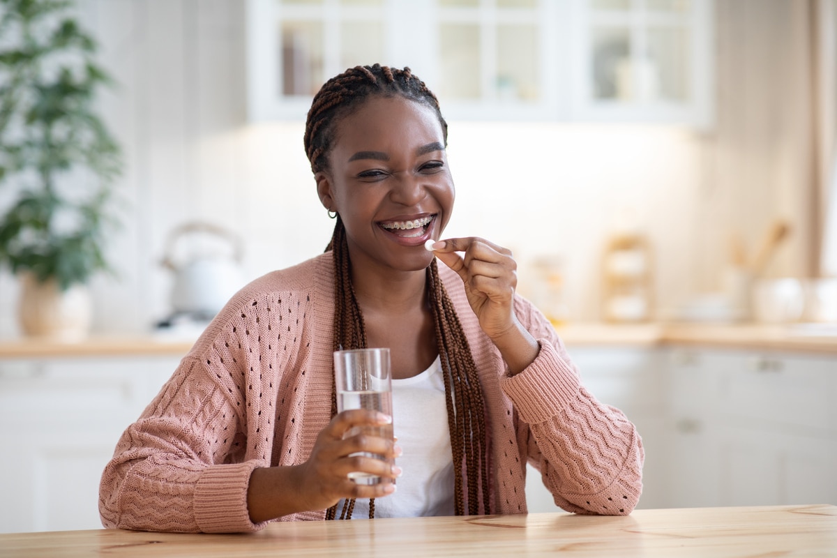 beauty supplements. positive black female taking vitamin pill and water at home