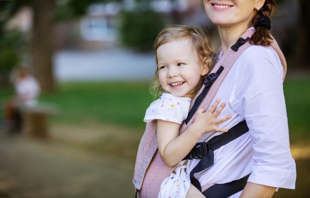 caucasian woman and her daughter in baby carrier in park