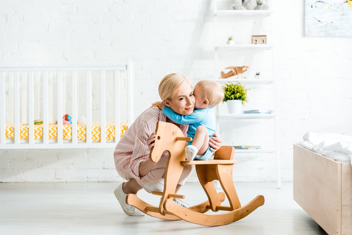 cute toddler son hugging happy blonde mother near rocking horse