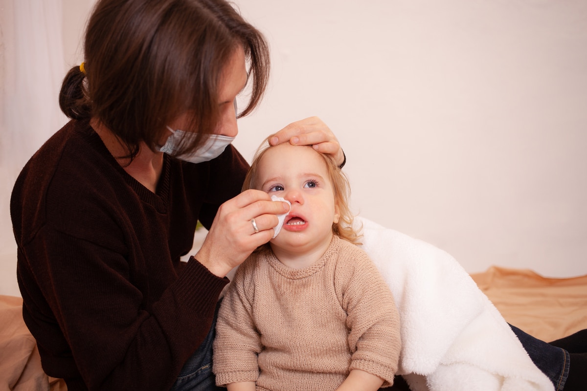 dad in a mask wipes his daughter's nose. the child's snot, empty space for text. colds, flu, home quarantine, sick