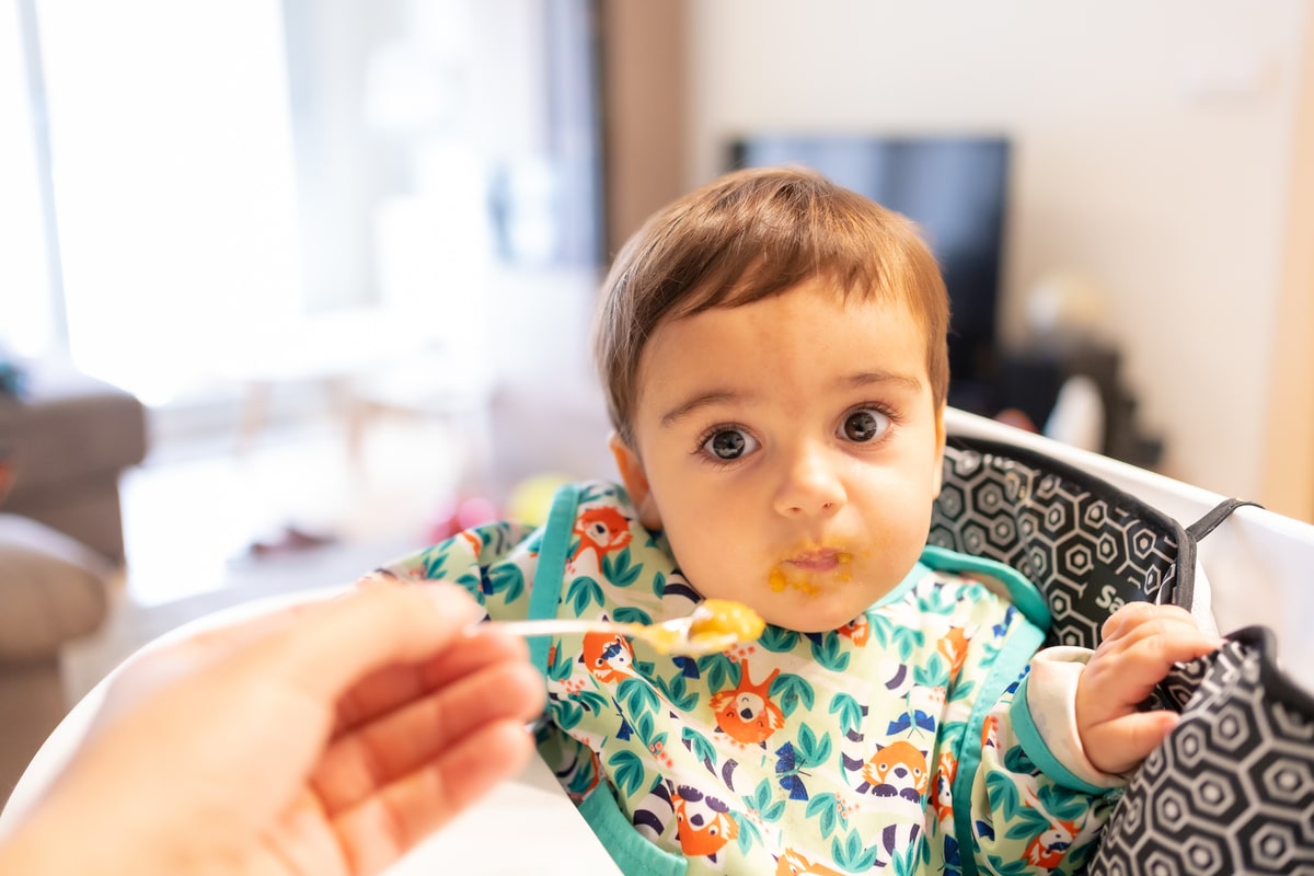 father feeding his baby solid food, his first vegetable purees