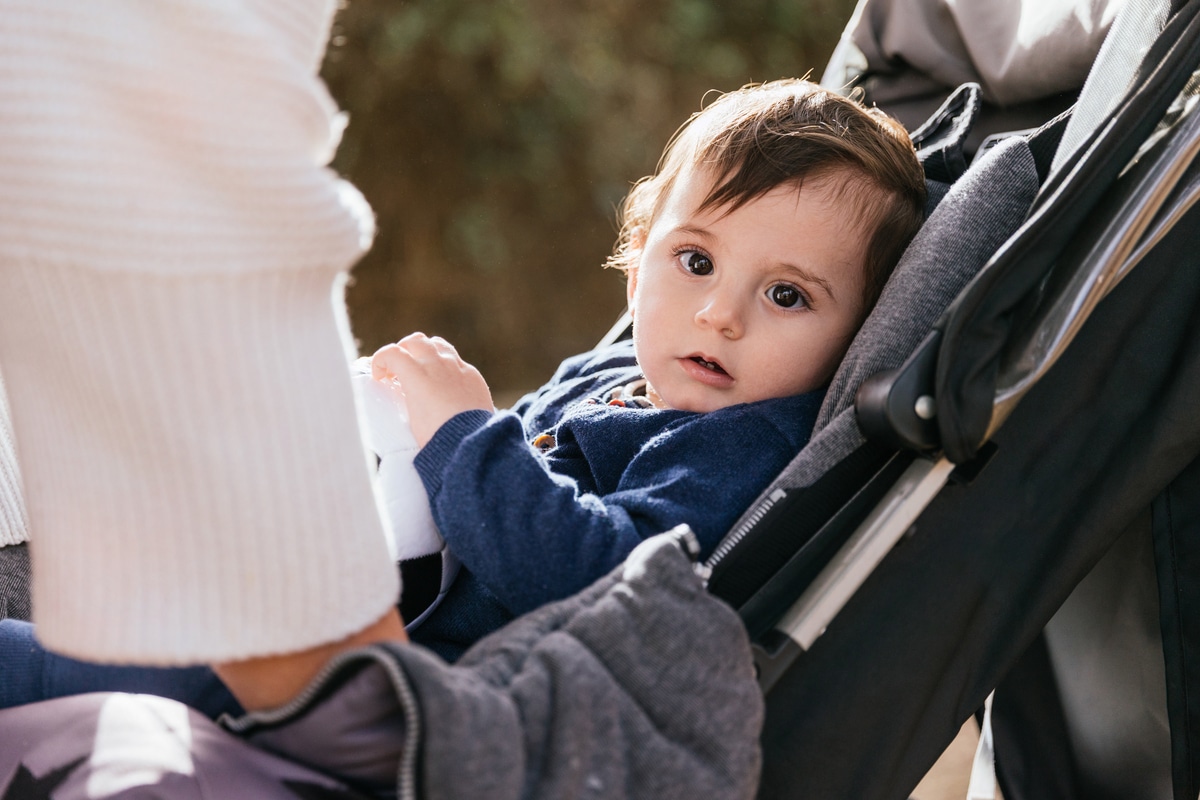 little kid looking at camera while sitting in the stroller pram outdoors.