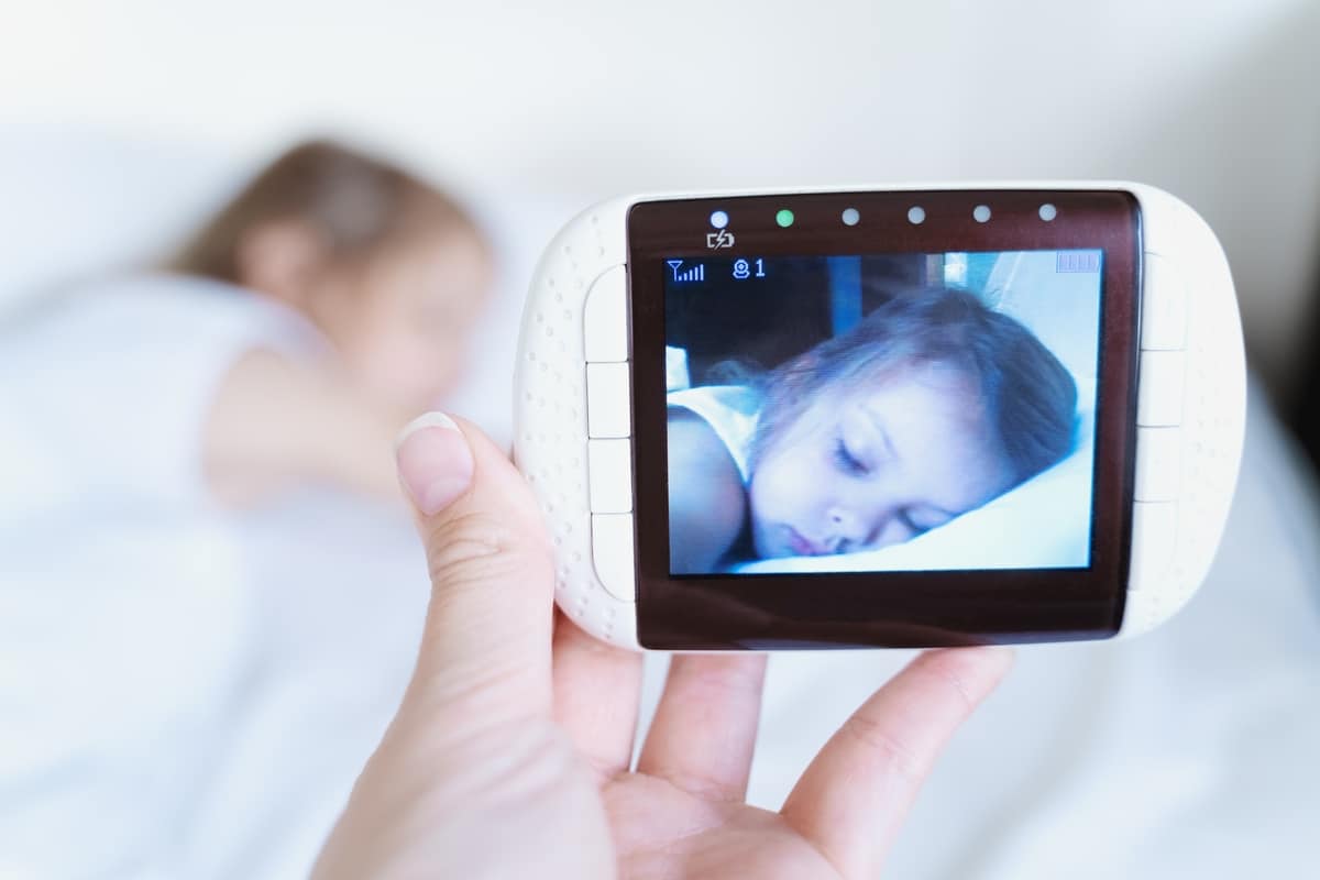 mom looks at the camera for a little sleeping girl, daughter through the radio, video baby monitor. protection, care for the safety of the child. remote control of the soap. modern technologies