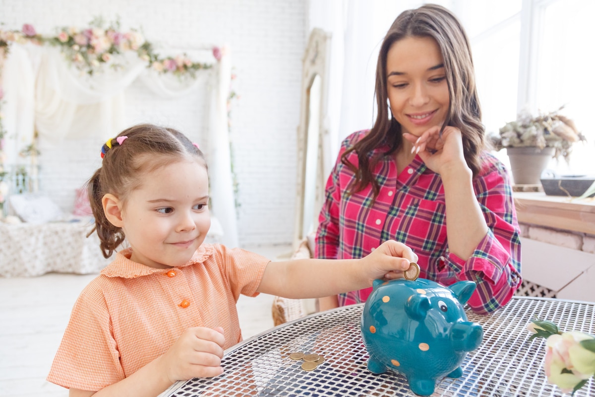 mom teaches a little daughter to collect money in a piggy bank.
