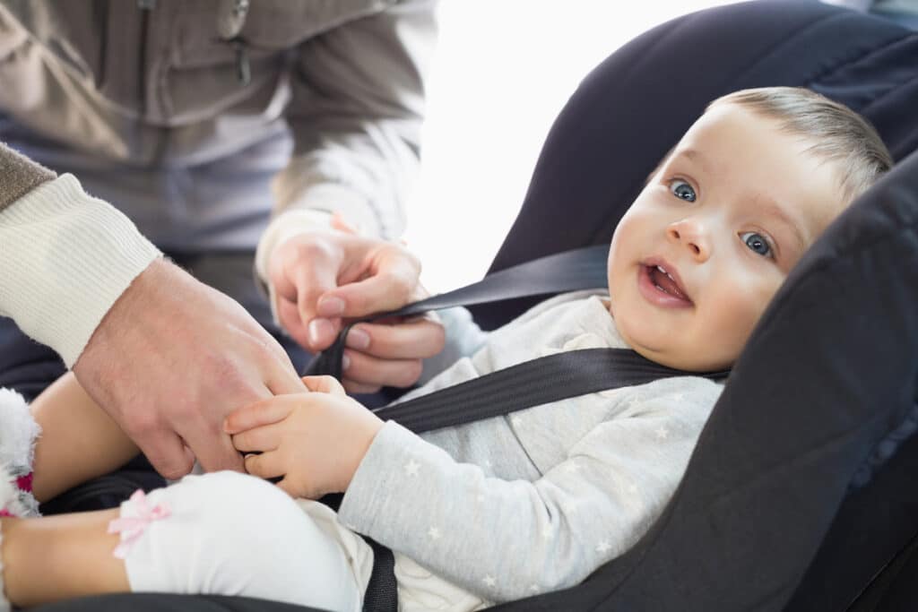 parents securing baby in the car seat in his car