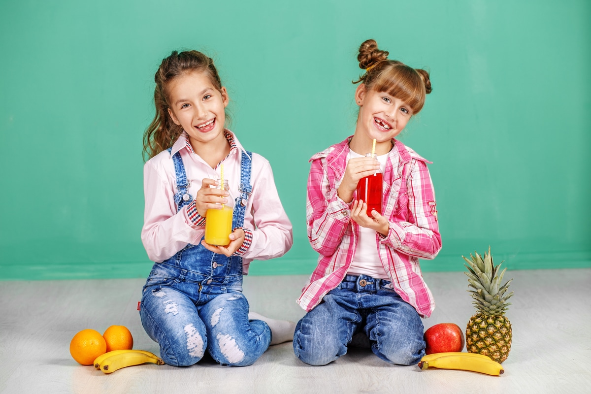 two children drink orange and pomegranate juice. girls in jeans.