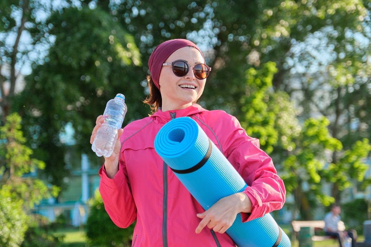 mature woman in sports windbreaker with yoga mat bottle of water, walking outdoor