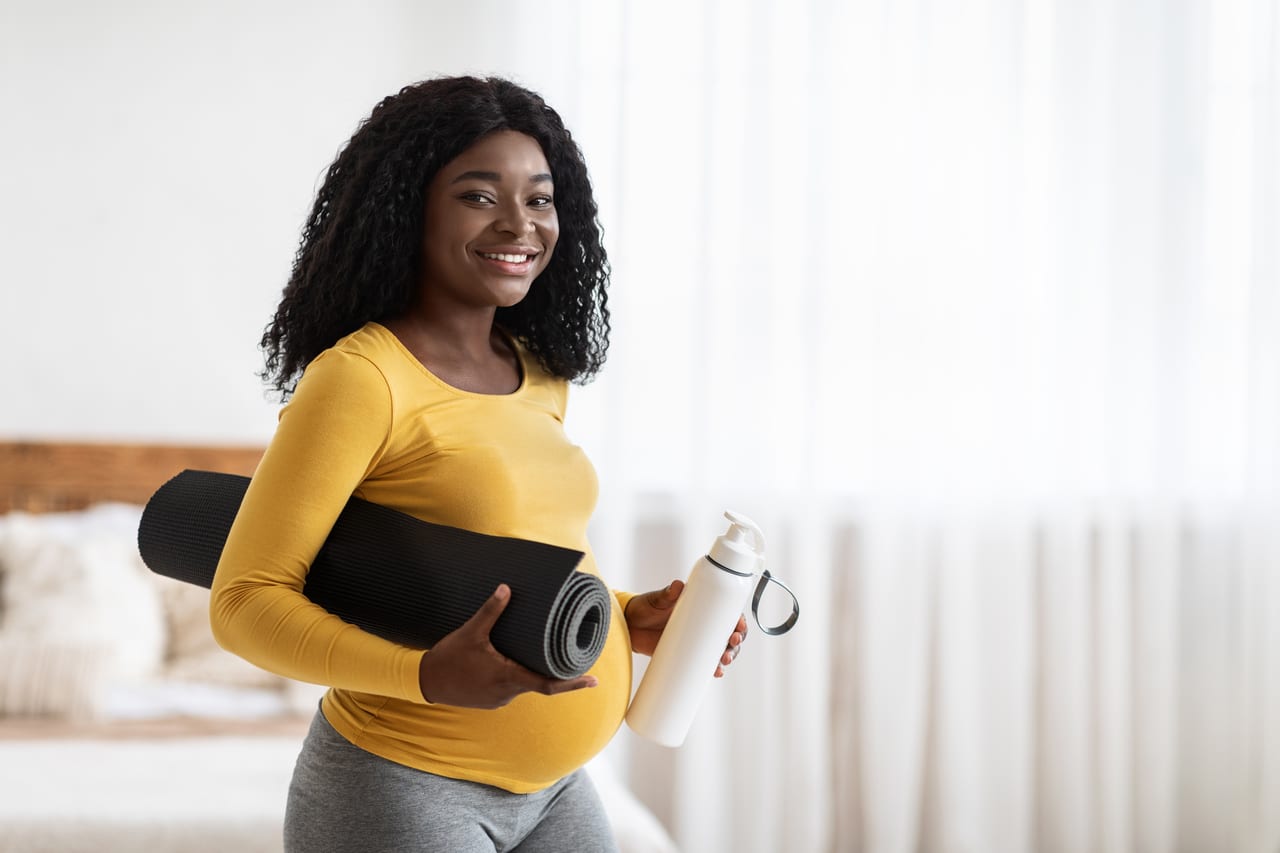 happy pregnant woman with yoga mat and bottle of water